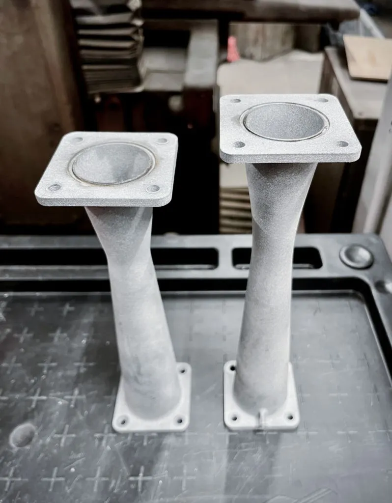 Dwie polimerowe zwężki układu dolotowego do bolidu, wydrukowane w technologii 3D, prezentujące precyzyjne kołnierze montażowe i gładkie przejścia wewnętrzne.