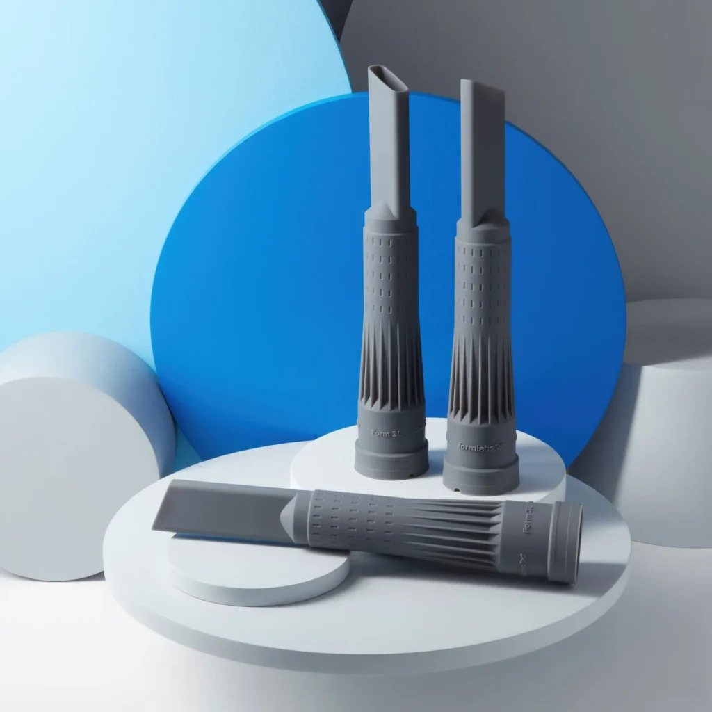 Trzy szare komponenty techniczne o złożonej geometrii, wydrukowane precyzyjnie w technologii 3D SLA z żywicy.