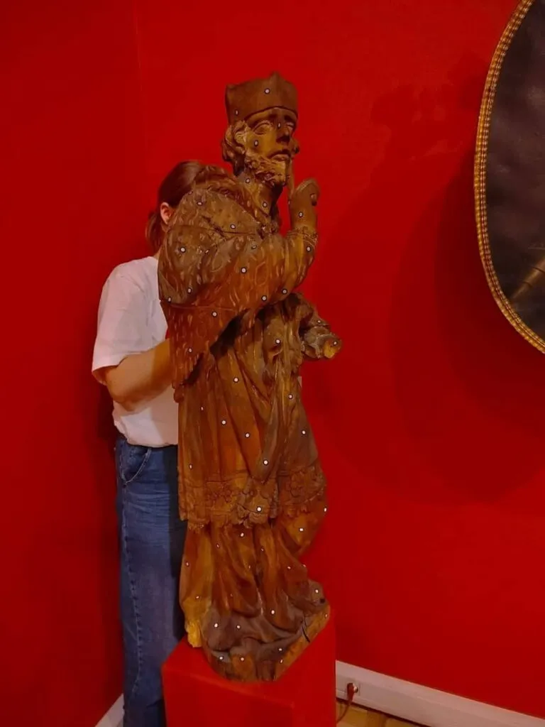 Zabytkowa drewniana rzeźba na czerwonym tle, przygotowana do skanowania 3D w Muzeum Ziemi Lubuskiej.